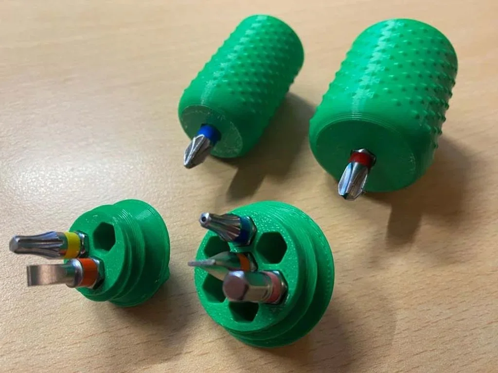 Vier grüne 3D-gedruckte Bit-Halter mit Noppen-Griff und eingesetzten Schraubendreher-Bits, daneben die offenen Kappen mit Sechskant-Aufnahmen